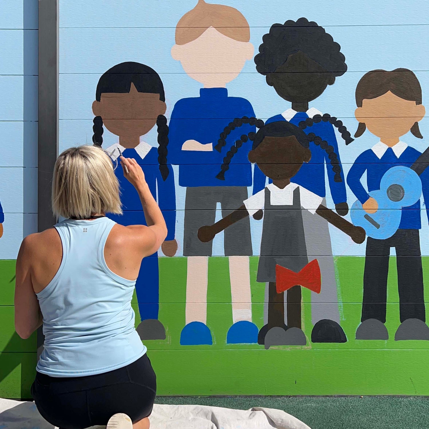 woman painting a mural of a diverse range of school children
